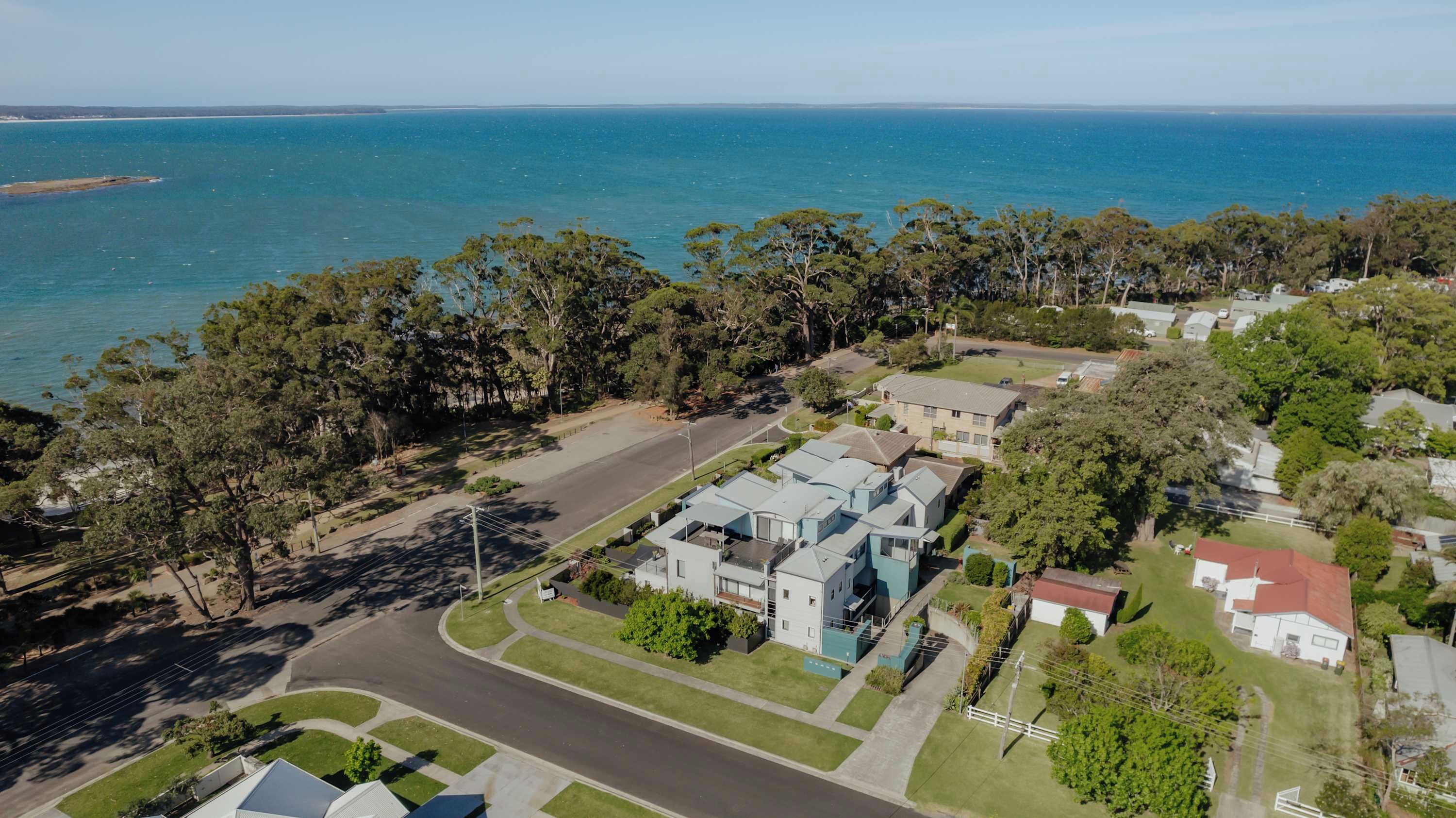 An aerial view of a coastal residential area with houses, a road, and a beach.