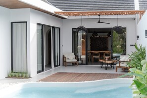 A modern outdoor pool area with a wooden deck, seating, and a glass-enclosed patio. - Wild Paradise Villa - 2 Bedrooms (Pecatu)