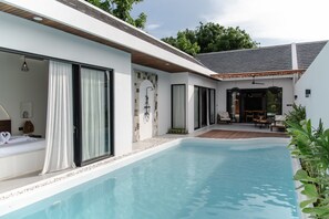 A modern poolside area with a clear pool, a wooden deck, and a seating area with a table and chairs. - Wild Paradise Villa - 2 Bedrooms (Pecatu)