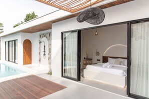 A modern bedroom with a large bed, a glass door leading to a balcony, and a pool area. - Wild Paradise Villa - 2 Bedrooms (Pecatu)