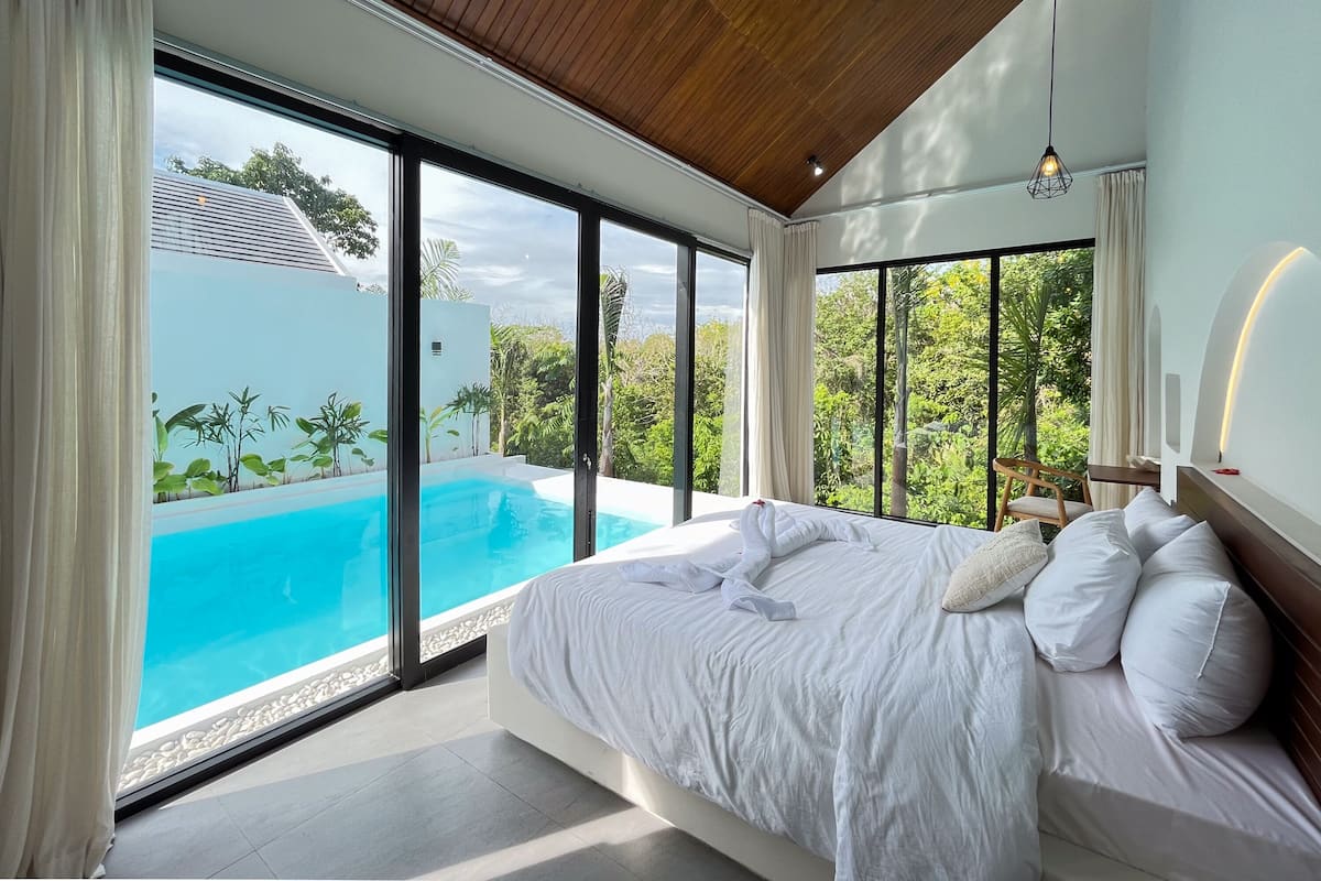 Ein Schlafzimmer mit einem großen Bett, Blick auf einen Swimmingpool und einer Holzbalkendecke.