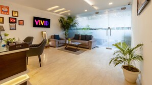 A modern reception area with a reception desk, seating area with a sofa and chairs, a large potted plant, and a 'VIVID' sign on the wall. - Vivid Boutique Hotel, Medanta, Gurugram (Gurugram)