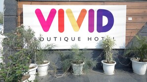 A sign for 'VIVID Boutique Hotel' with a colorful logo and potted plants in front. - Vivid Boutique Hotel, Medanta, Gurugram (Gurugram)
