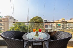 A round glass table with wicker chairs on a balcony overlooking a cityscape. - Vivid Boutique Hotel, Medanta, Gurugram (Gurugram)