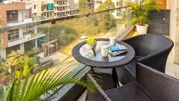 A balcony with wicker furniture, a glass table, and a potted plant. - Vivid Boutique Hotel, Medanta, Gurugram (Gurugram)