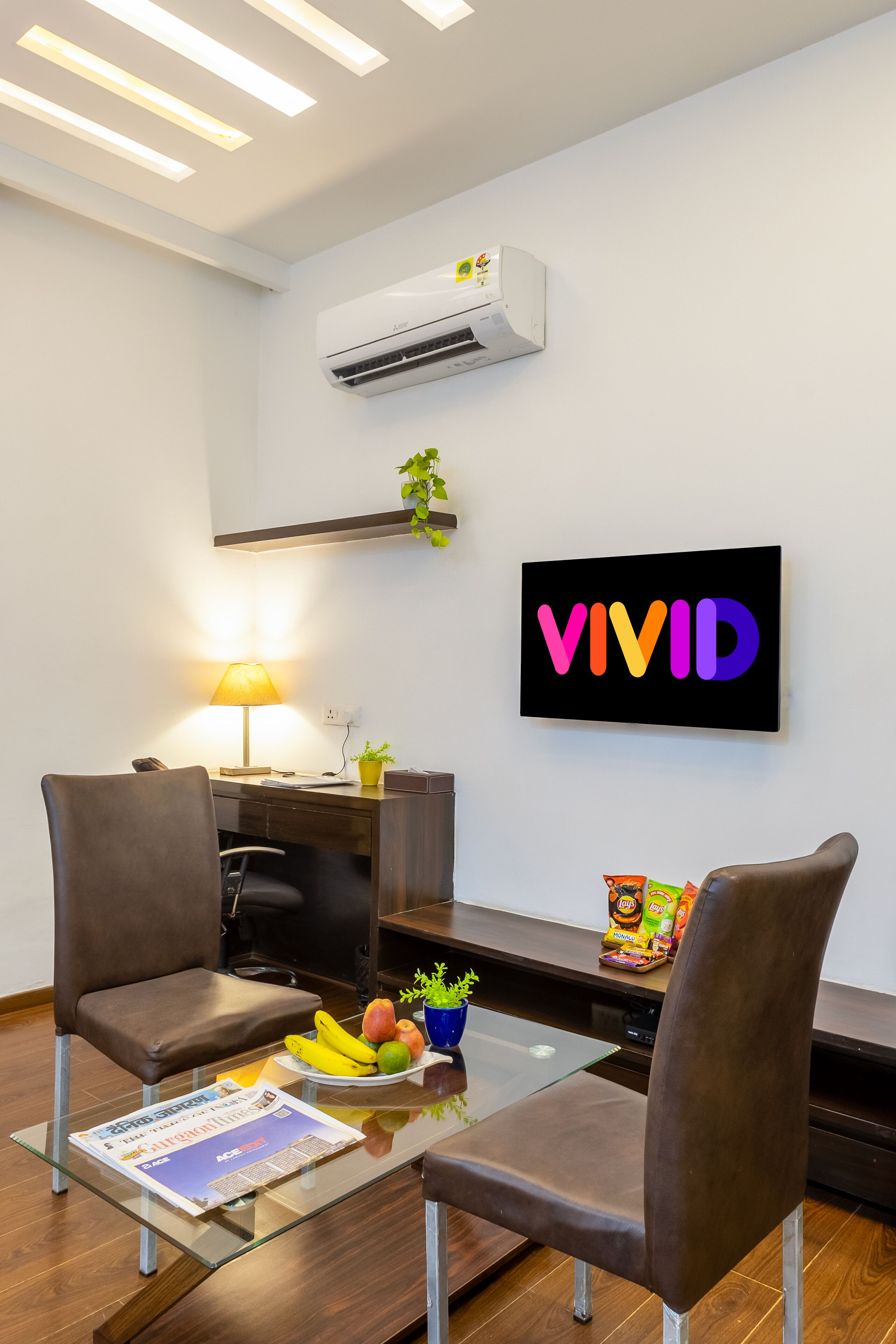 A modern office space with two brown chairs, a glass table with a magazine, a bowl of fruit, and a VIVID sign on the wall.
