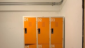 A row of orange lockers with labels D1 to D8, a wooden floor, and a white wall with a black pipe.