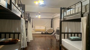 A dormitory-style room with bunk beds, a ceiling fan, and a window with curtains.