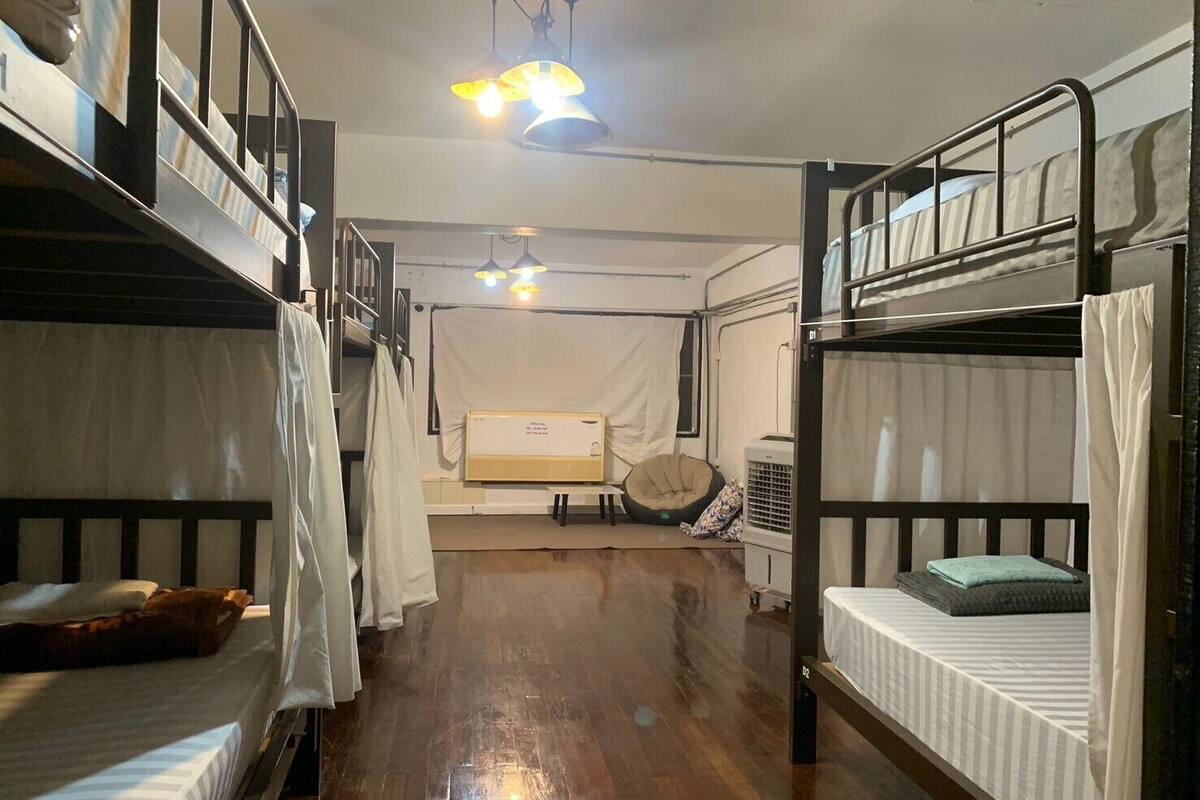 A dormitory-style room with bunk beds, a ceiling fan, and a window with curtains.