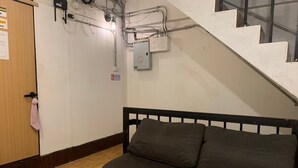 A room with a wooden door, a black bench, a round container, and a staircase.