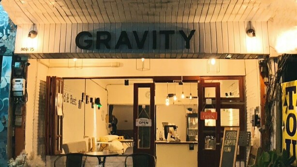 A restaurant named 'GRAVITY' with an open sign, outdoor seating, and a chalkboard menu.