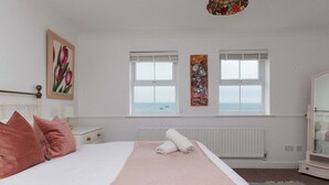 A bedroom with a bed, two windows, a radiator, a nightstand, and a dresser. - Spacious 4-Bed Seaside Retreat in Selsey (Selsey)