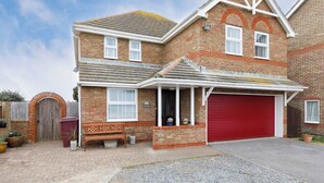 A two-story brick house with a red garage door, a wooden bench, and a brick wall with a window. - Spacious 4-Bed Seaside Retreat in Selsey (Selsey)