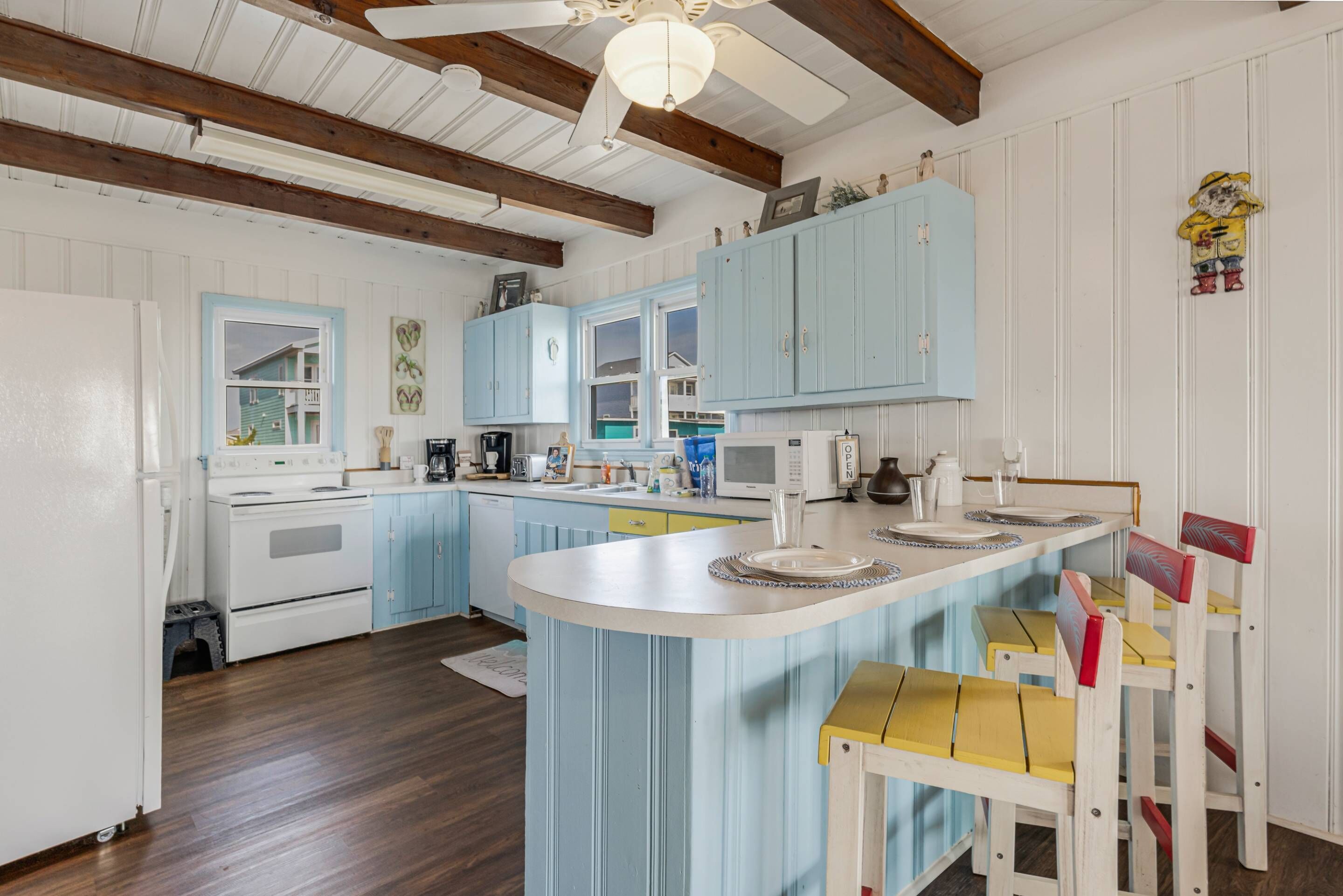 A kitchen with light blue cabinets, a white island, wooden chairs, and a ceiling fan.