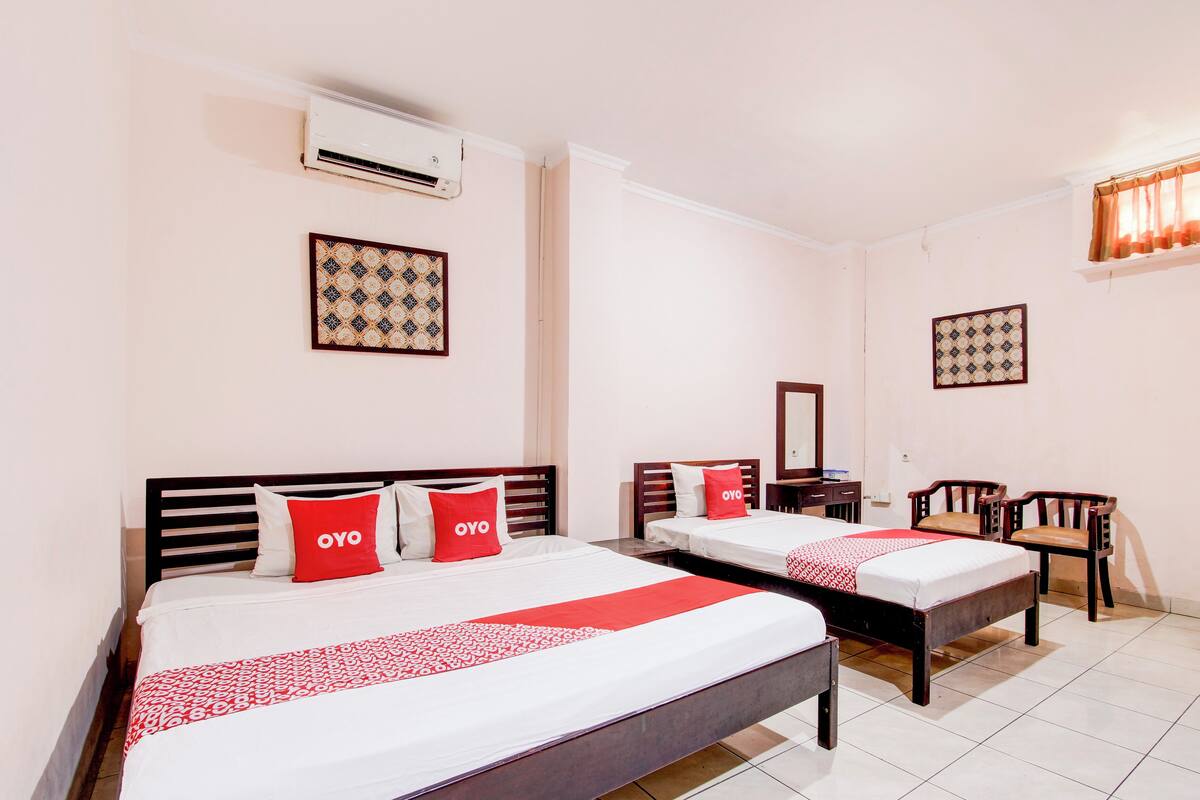 A hotel room with two beds, each with a red and white bedspread, a mirror, a desk, and two chairs.