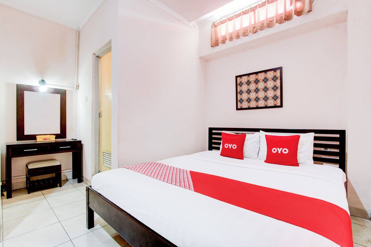 A hotel room with a bed, a desk, a mirror, and a window with curtains.