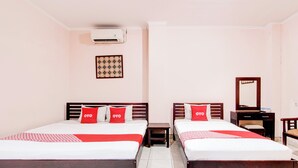 A hotel room with two beds, each with a wooden frame, white bedding, and red pillows. There is a small bedside table with a lamp, a mirror on the wall, and a patterned artwork above the left bed. - Collection O Simpang Lima Near Simpang Lima Semarang Formerly Hotel Eben Haezer (Semarang)