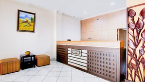A reception area with a wooden reception desk, two cushioned seating areas, a framed landscape painting, and a decorative metal panel. - Collection O Simpang Lima Near Simpang Lima Semarang Formerly Hotel Eben Haezer (Semarang)