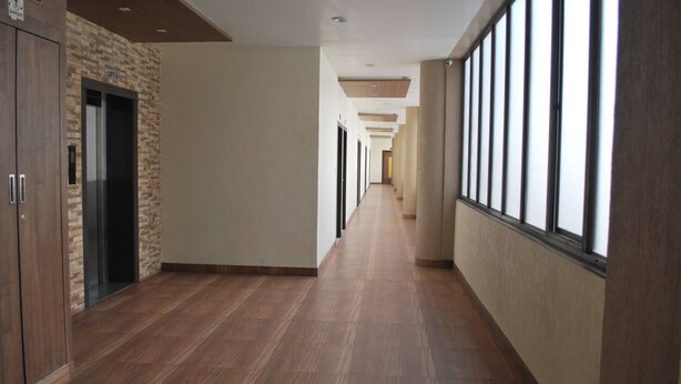 A long, narrow hallway with wooden flooring and large windows on one side. - Hotel Vijya laxmi Rooms and Banquet Hall (Surat)