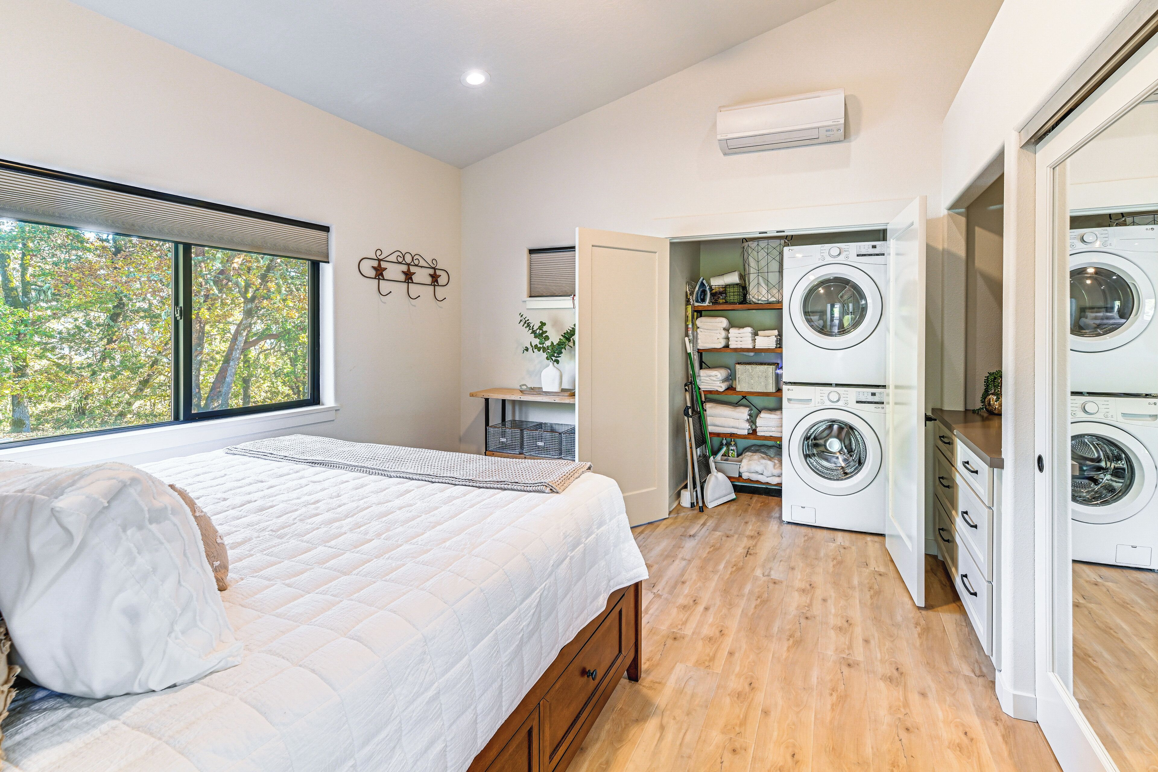 Une chambre avec un grand lit, une fenêtre donnant sur la verdure et un espace buanderie équipé de deux machines à laver.