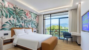 Een moderne hotelkamer met een groot bed, nachtkastje, televisie en balkon met uitzicht op de bergen.
