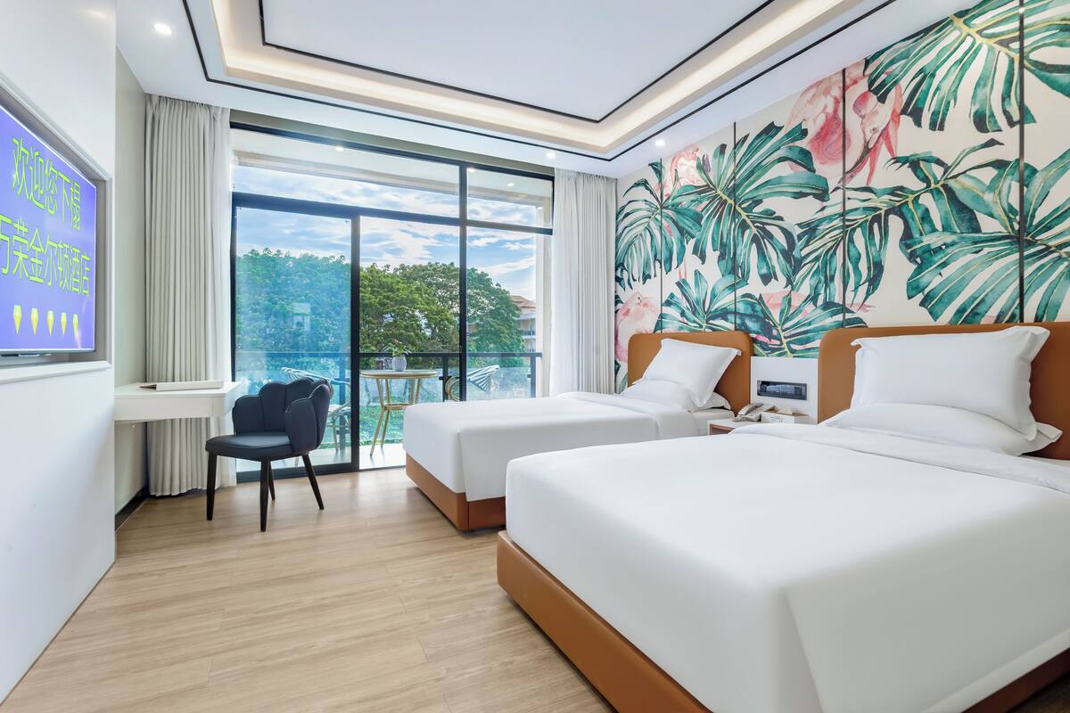 A hotel room with two beds, a desk with a chair, a large window with a view, and a tropical-themed wall mural.