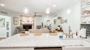 A modern kitchen with a large island, pendant lights, a fireplace, and a dining area with a sofa.