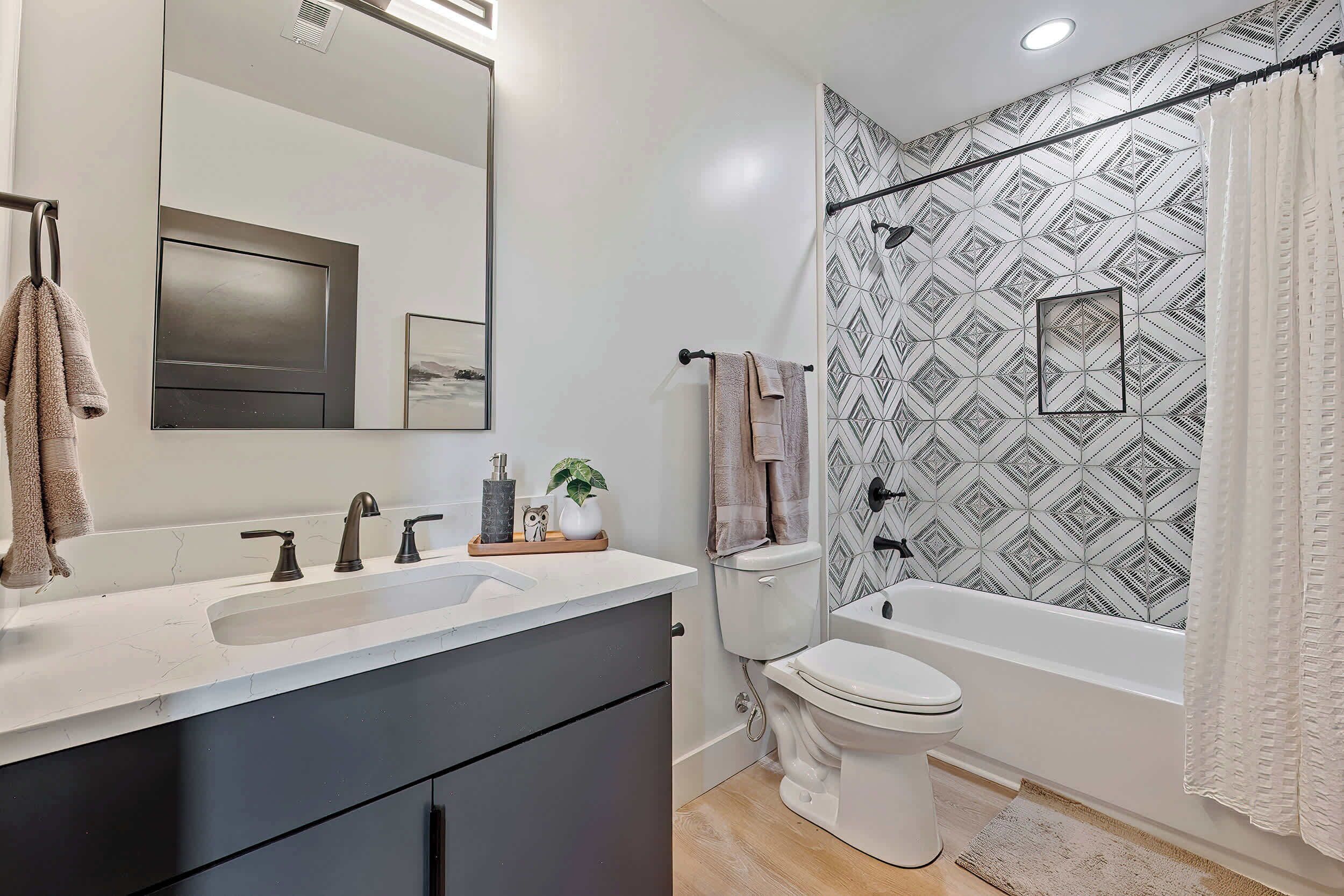 A modern bathroom with a large mirror, two sinks, a toilet, and a bathtub.