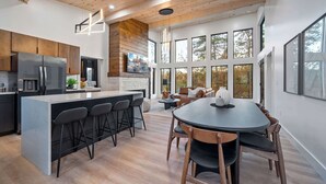 A modern kitchen with a central island, bar stools, and a dining area with a round table and chairs. - Luxury 3 Br Cabin~Indoor Pool~Hot Tub~Fire Pit (Sevierville)