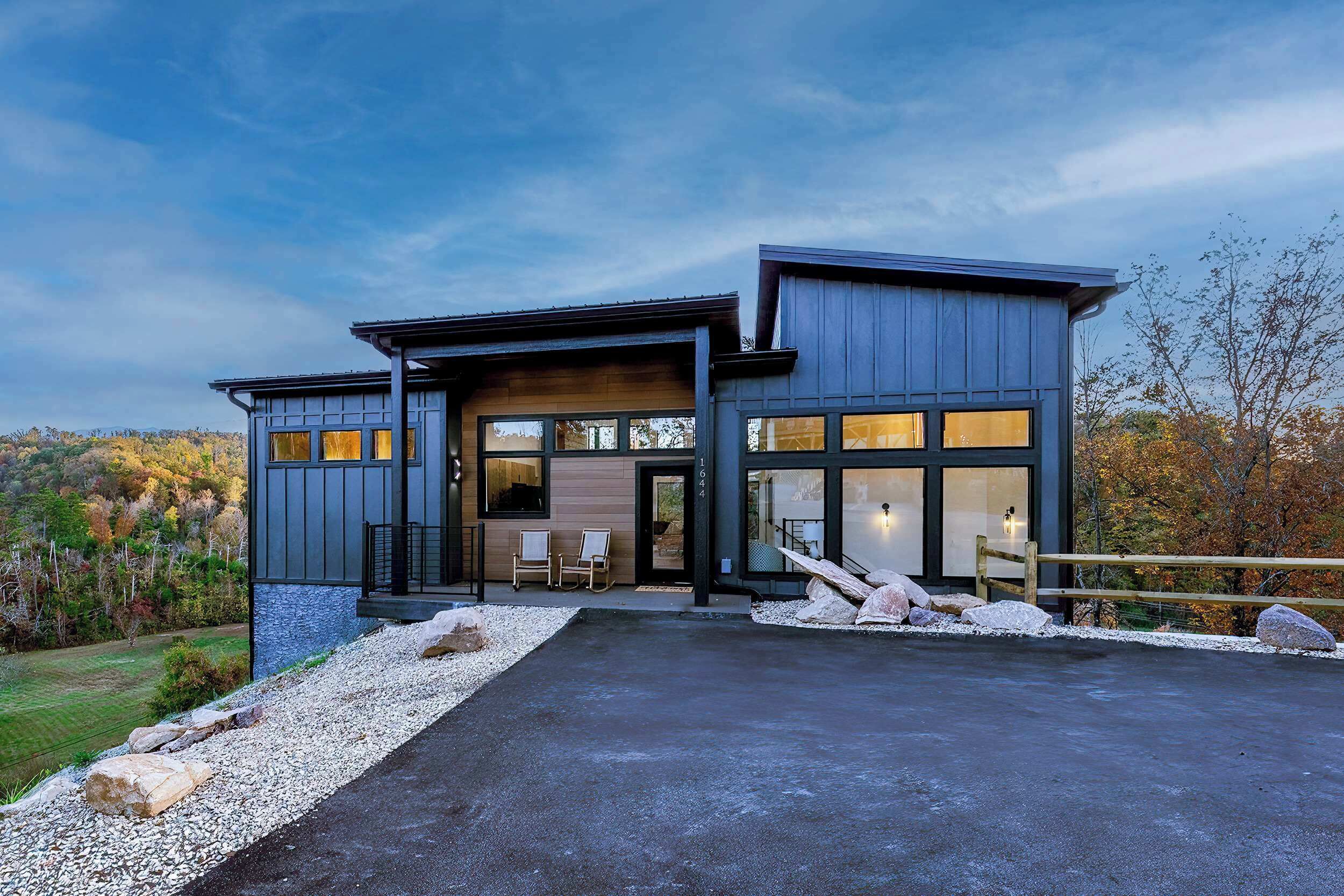 Ein modernes, zweistöckiges Haus mit einer großen Auffahrt, einer Sitzgelegenheit im Freien und Blick auf die umliegende Landschaft.