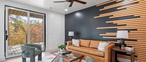 A modern living room with a sofa, two chairs, a coffee table, and a ceiling fan.