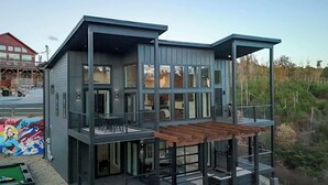 A modern two-story house with a balcony and a covered outdoor area. - Luxury 3 Br Cabin~Indoor Pool~Hot Tub~Fire Pit (Sevierville)