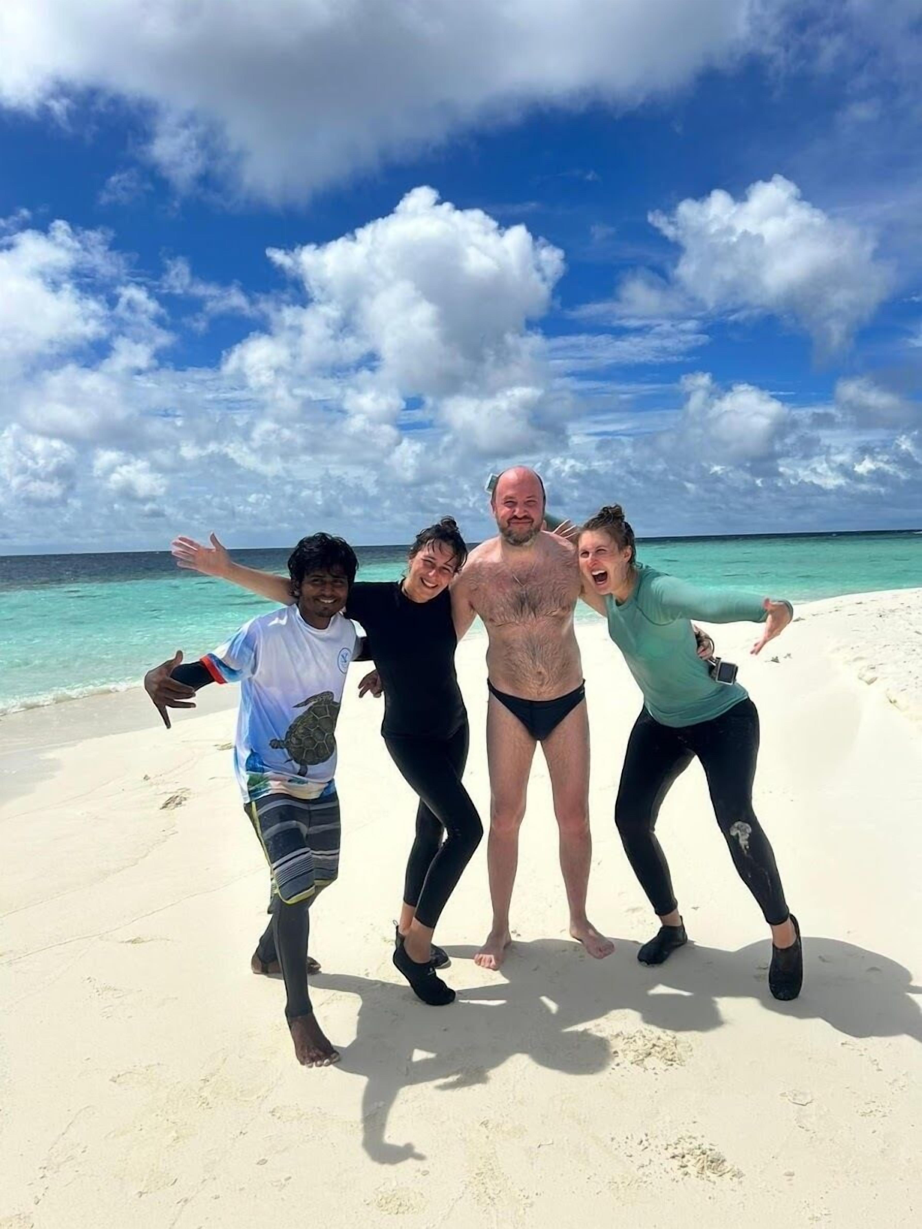 A group of people on a sandy beach with a clear sky and ocean in the background.