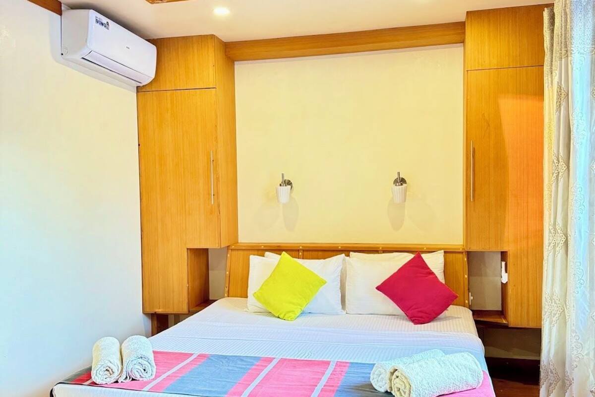 Une chambre d’hôtel avec un lit en bois, un ventilateur de plafond, un appareil de climatisation et des armoires en bois.