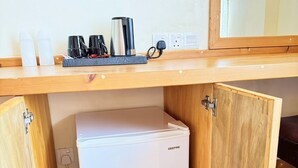 A compact kitchenette with a white GEEPAS mini-fridge, a coffee maker, and a kettle on a wooden countertop.