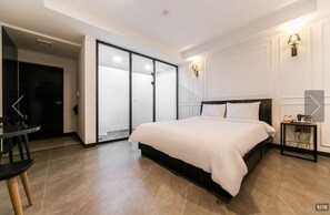 A modern bedroom with a large bed, a desk, and a sliding door leading to a bathroom.