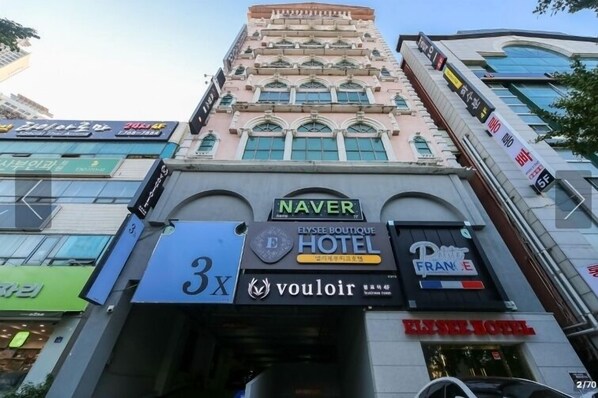 A hotel with a prominent 'NAVER' sign, '3X' branding, and 'vouloir' logo.