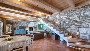 Un vaste espace de vie agrémenté d’un mur en pierre, de poutres apparentes en bois au plafond, d’un escalier et d’une table à manger avec des chaises.