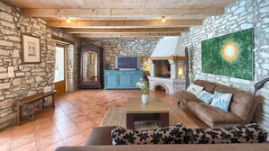 Un salon chaleureux avec des murs en pierre, un plafond en bois, une cheminée et un téléviseur.