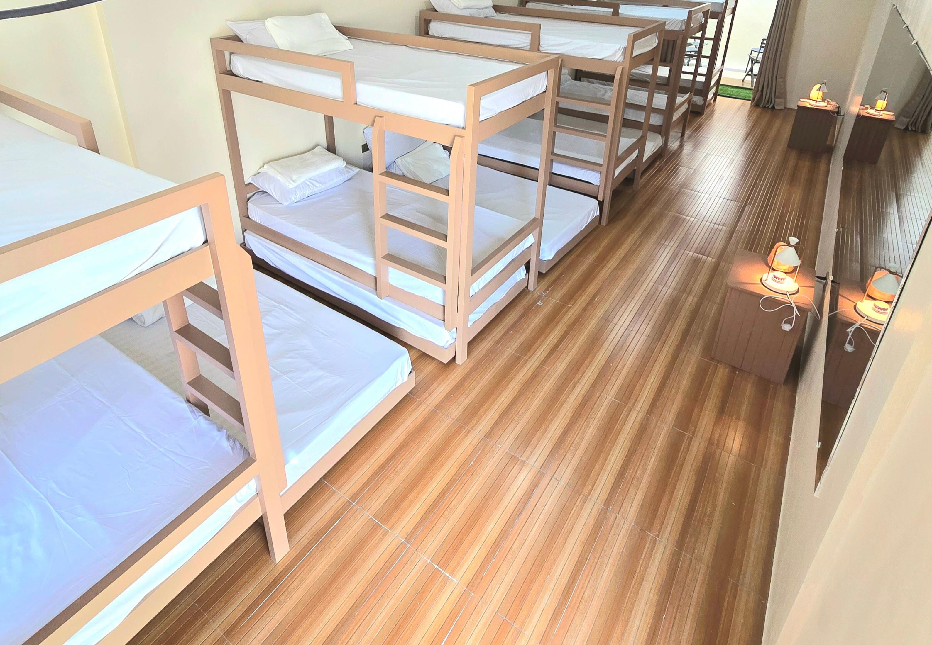 A row of bunk beds with wooden frames and white bedding, arranged in a dormitory-style room with a wooden floor.