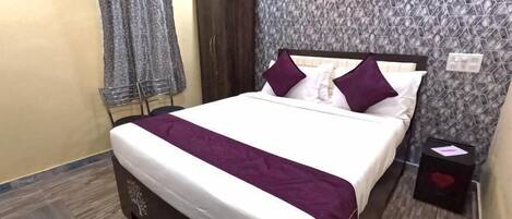 Una habitación de hotel ordenada con cama, mesita de noche, armario y una silla.
