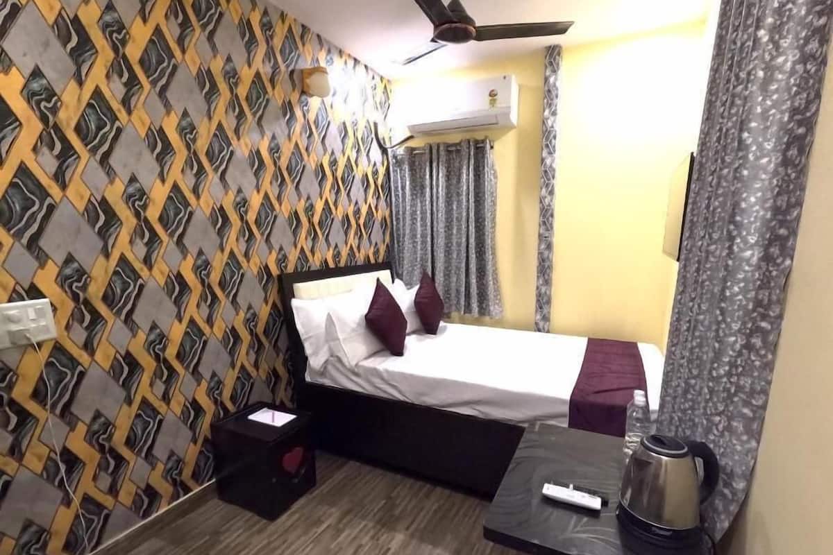 A hotel room with a bed, a bedside table with a kettle, a power outlet, and a patterned wall.