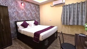 A hotel room with a bed, a desk, a chair, an air conditioning unit, and a patterned wall.