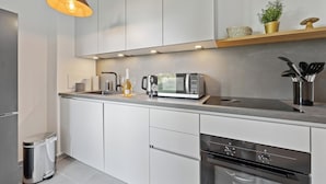 Una cocina moderna con gabinetes blancos, un refrigerador de acero inoxidable, un microondas y un horno.