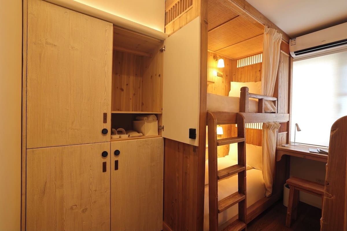 Un lit superposé en bois avec une échelle, un bureau et une chaise, dans une pièce aux murs et aux placards en bois.