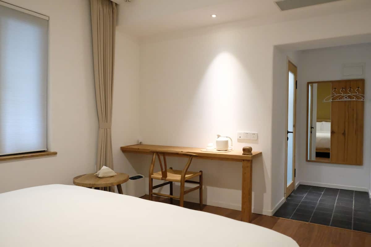 Une chambre d’hôtel avec un lit, un bureau en bois avec une bouilloire, une chaise et une petite table avec une boîte de mouchoirs.