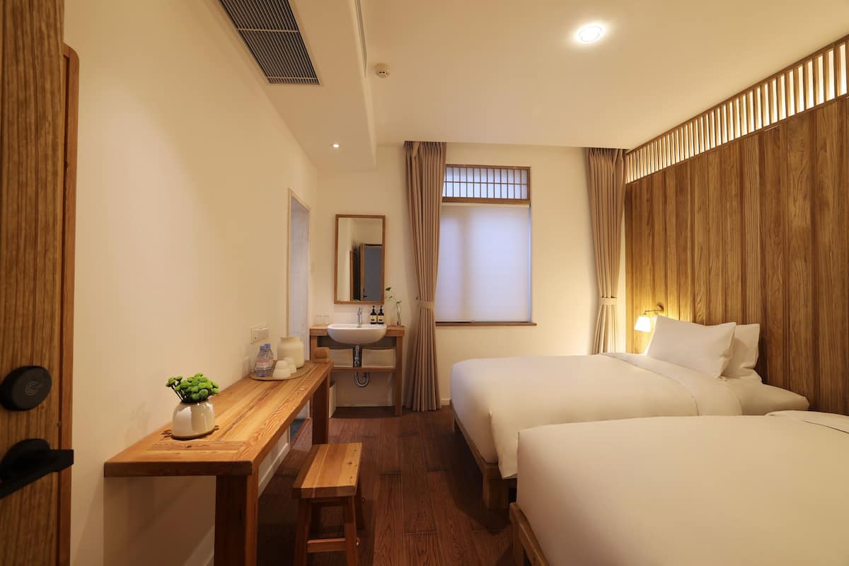 Une chambre d’hôtel avec deux lits, un bureau en bois orné d’une plante, un lavabo et un miroir.
