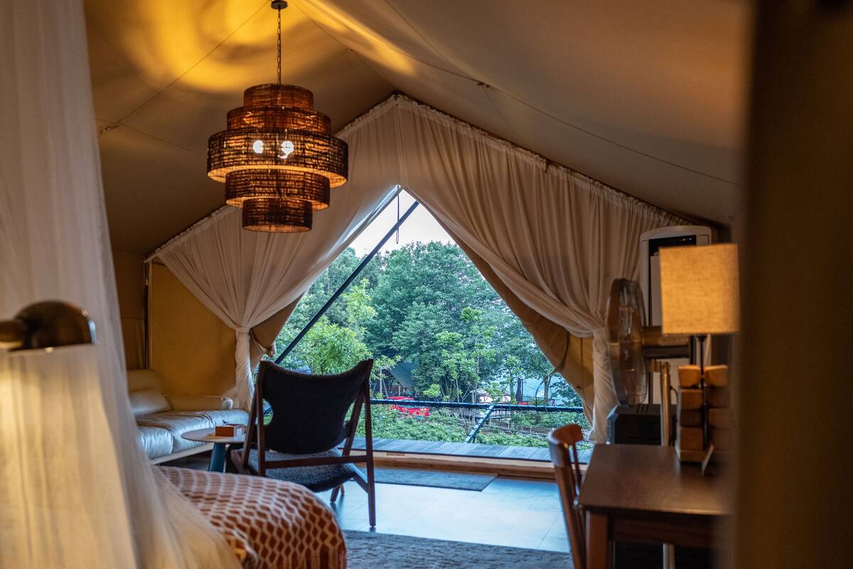 A tent-style room with a bed, a chair, a table, and a hanging light fixture.