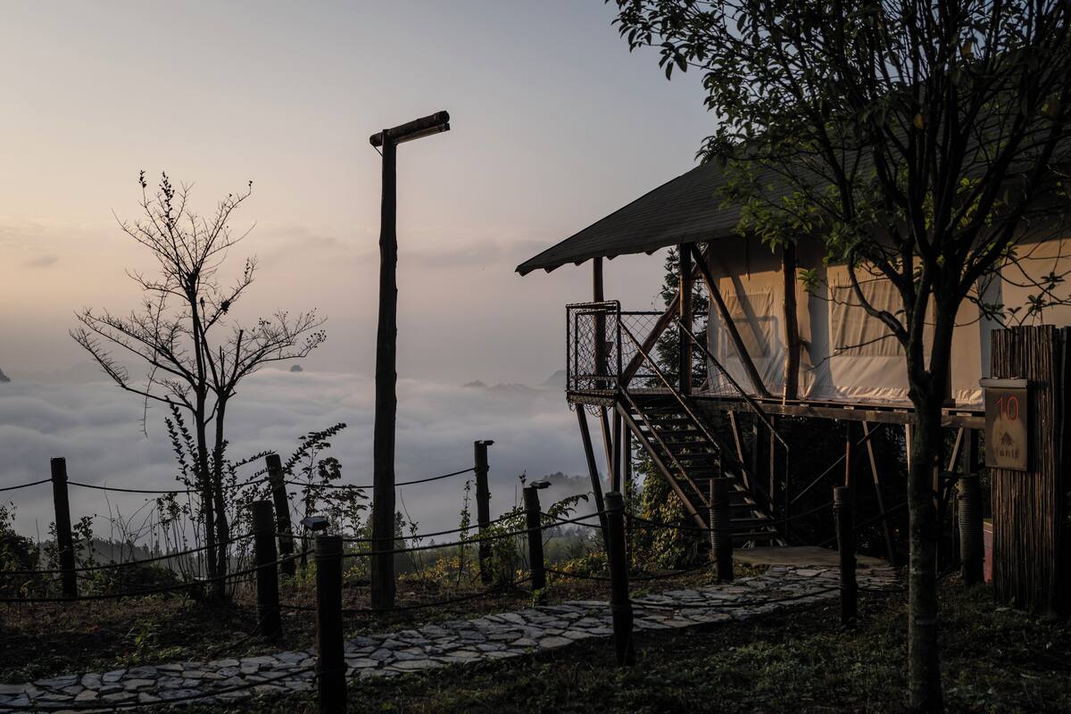 A rustic wooden structure with a balcony, surrounded by a stone pathway and a fence.