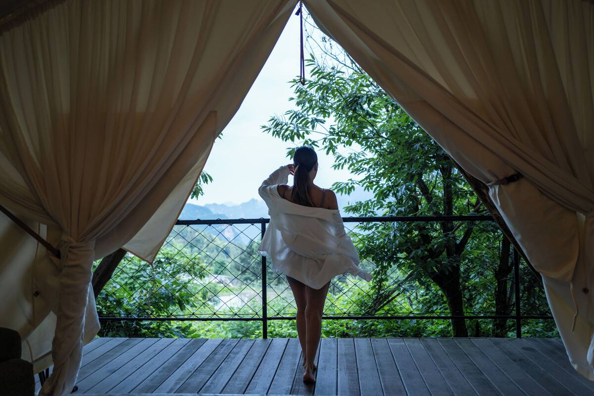 A person standing on a wooden deck with a view of greenery and mountains through a metal railing.
